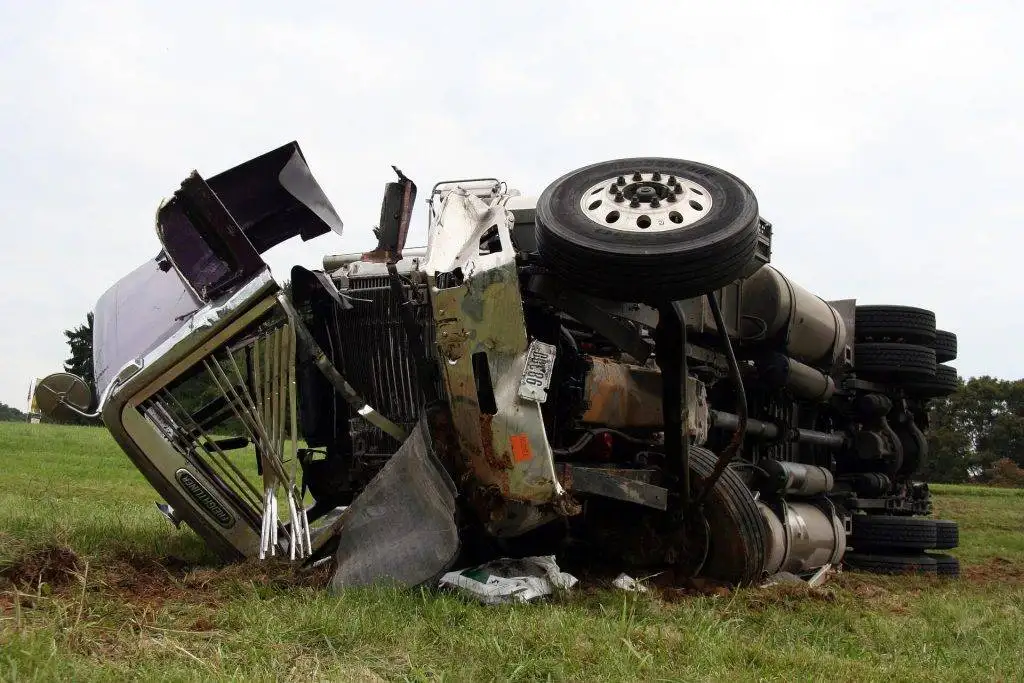 A crashed freight truck lying on its side in a grassy area