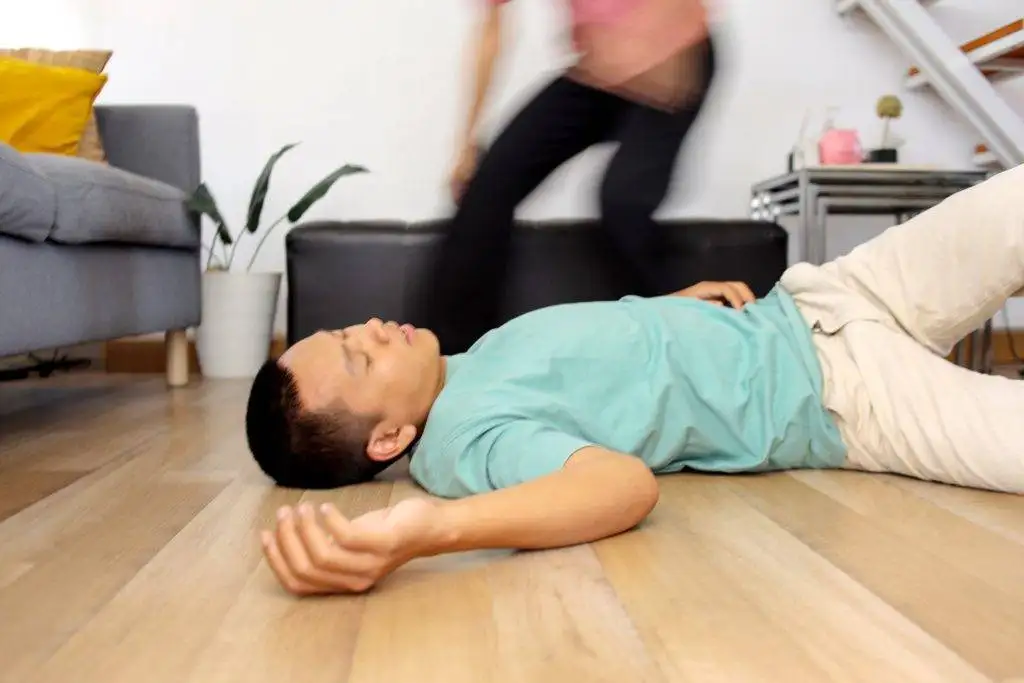 A man lies unconscious on the floor while a woman rushes to help him