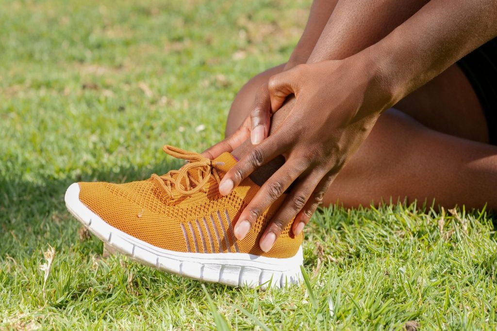 A person seated on grass clutches their ankle in discomfort