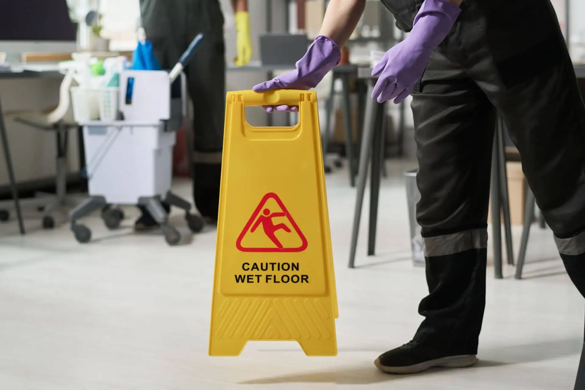 Cleaner placing a caution wet floor sign in an office