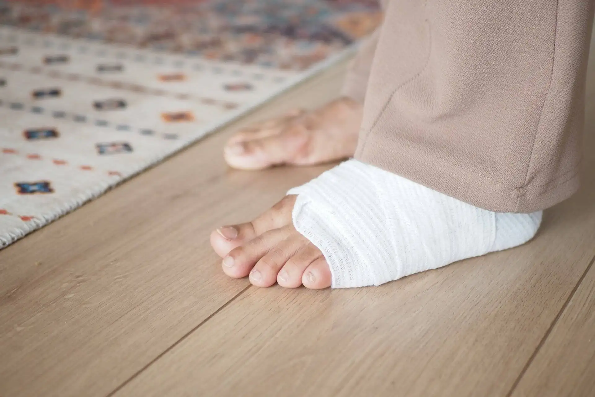 Close-up of a foot wrapped in a white bandage resting on a wooden floor