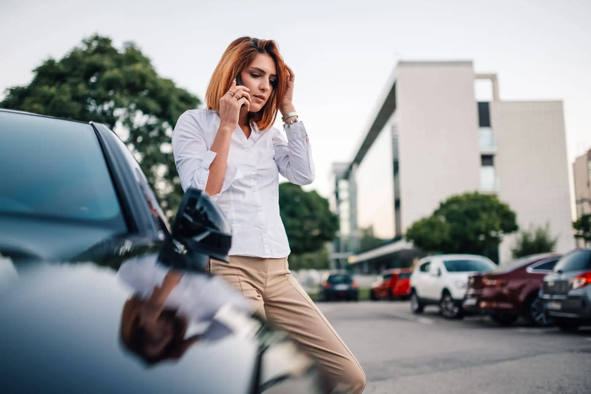Concerned woman talking on a smartphone next to her car in an urban parking area