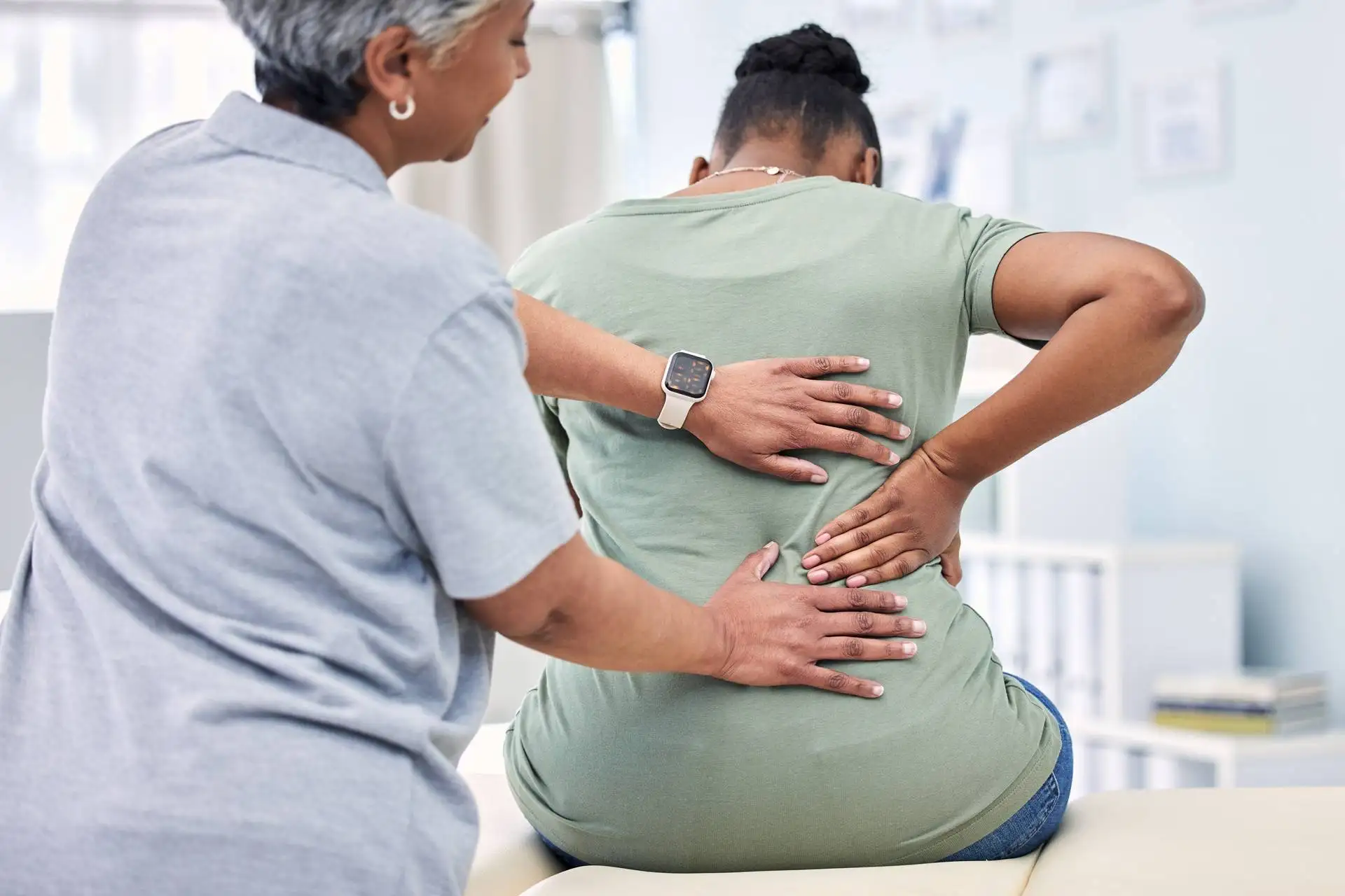 Female patient experiencing lower back pain being examined by a healthcare professional