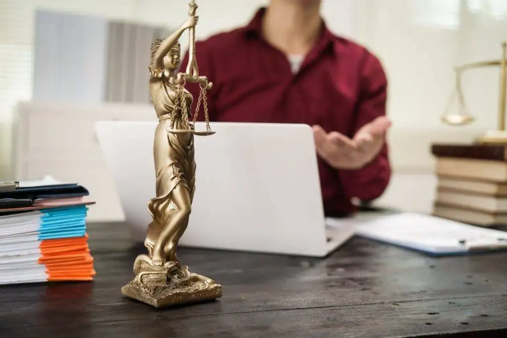 Justice statue on desk with lawyer in red shirt gesturing in background