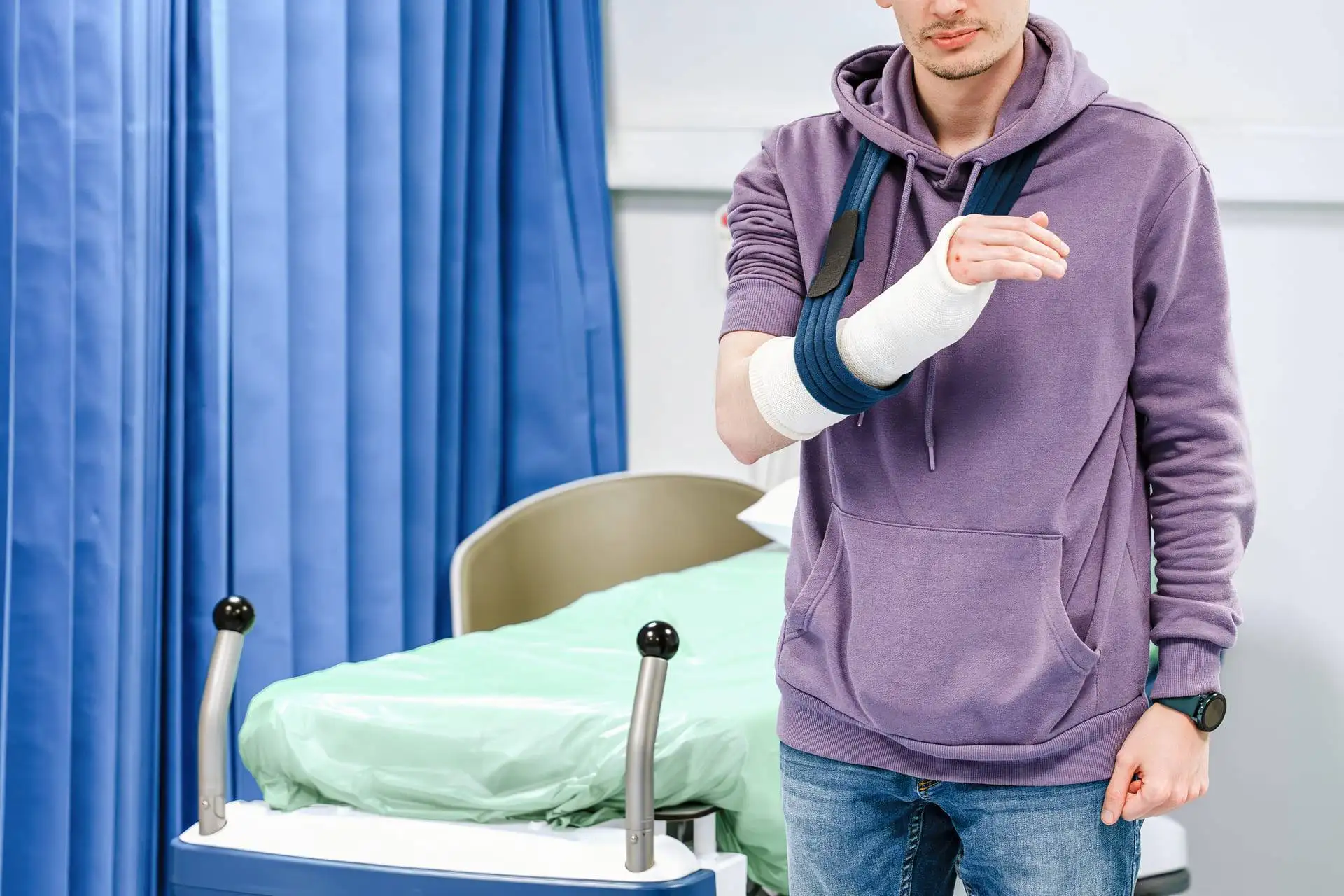 Man with a broken arm in a cast and sling standing in a hospital room