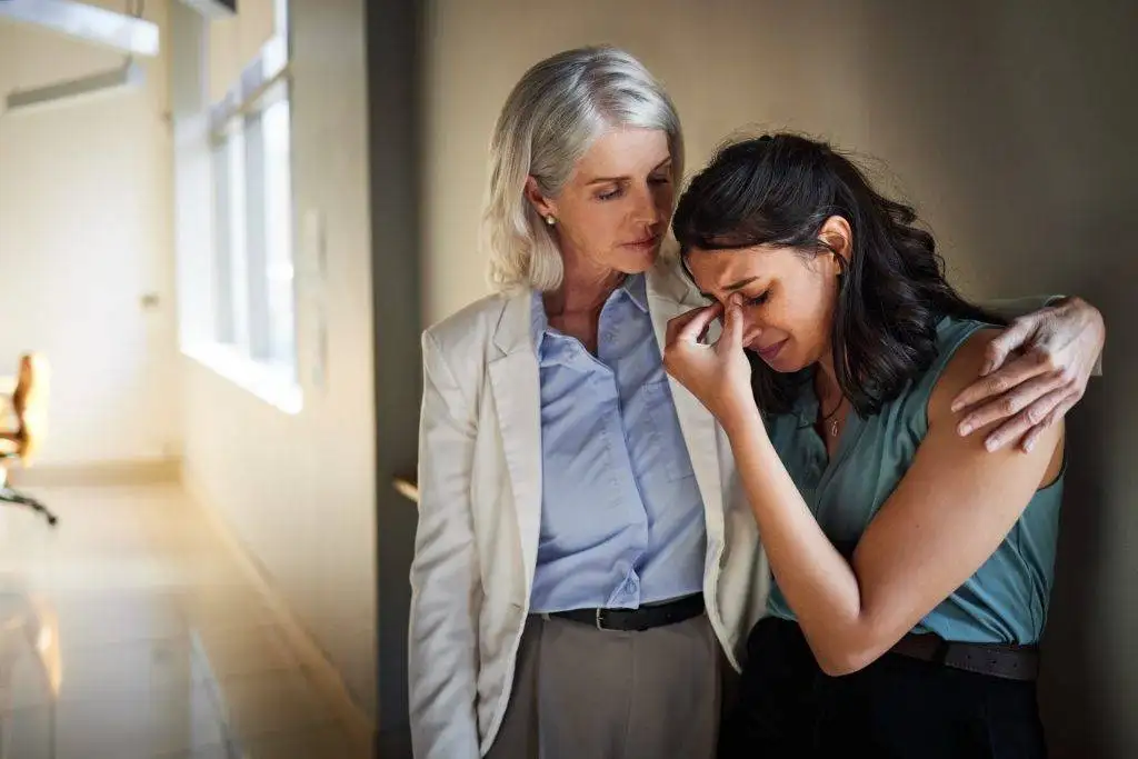 Older woman comforting younger crying woman in office hallway