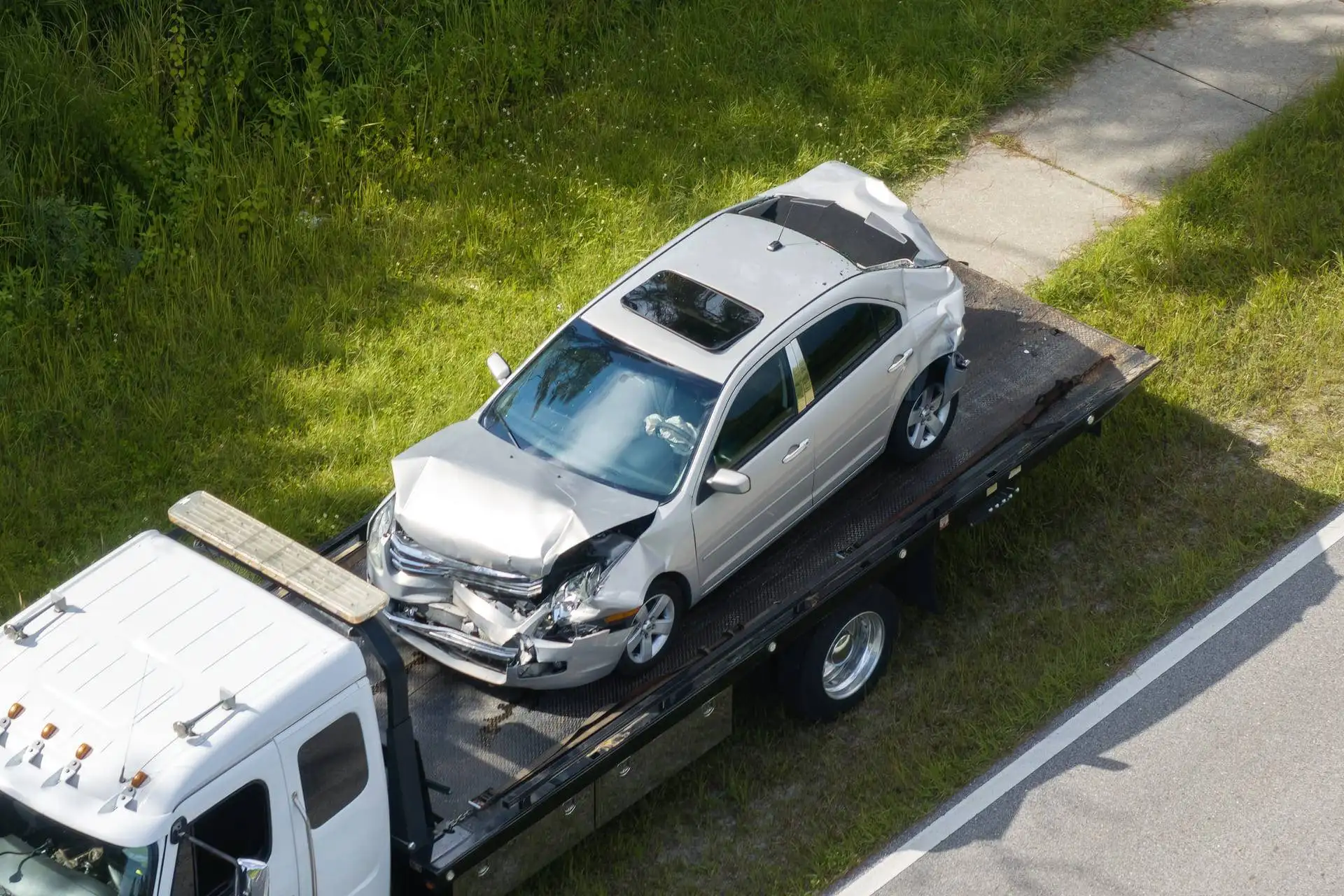 Silver car with severe front damage being transported on a tow truck