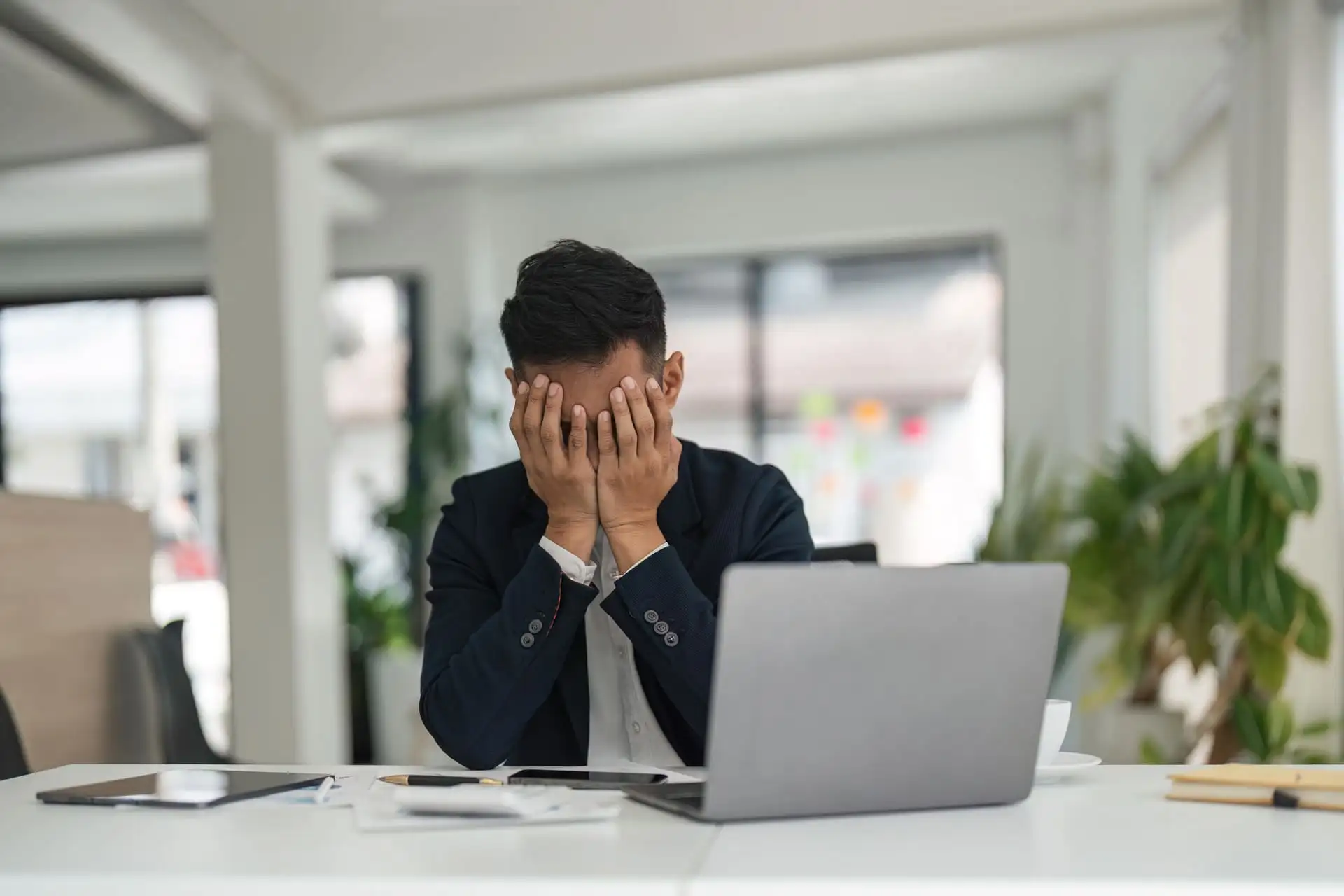 Stressed businessman covering his face in front of a laptop
