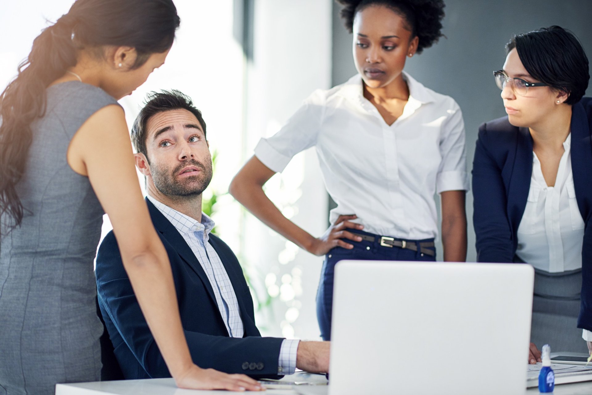 Three coworkers confronting a male colleague at a desk