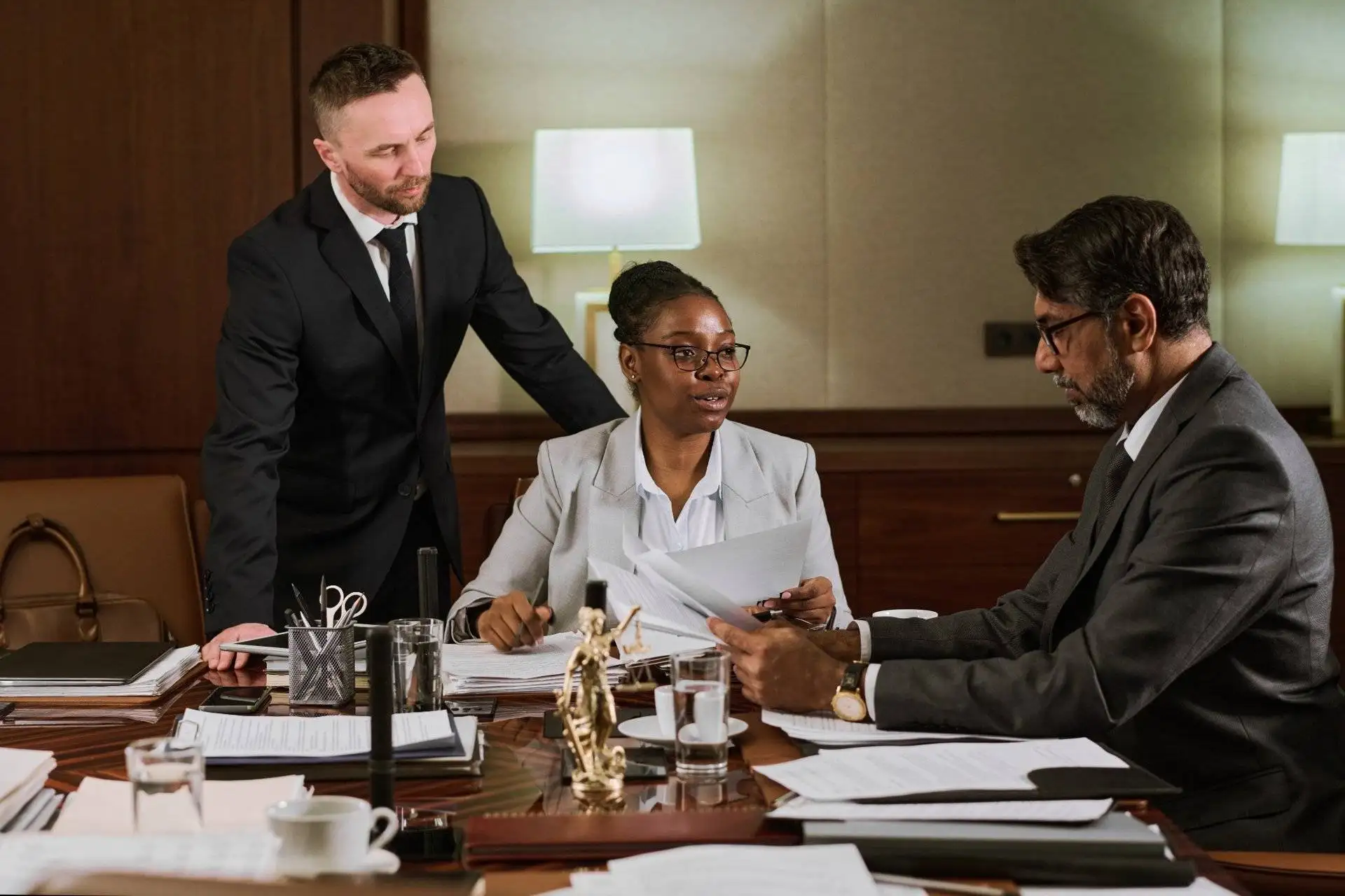 Three lawyers discussing paperwork in boardroom with Lady Justice statue