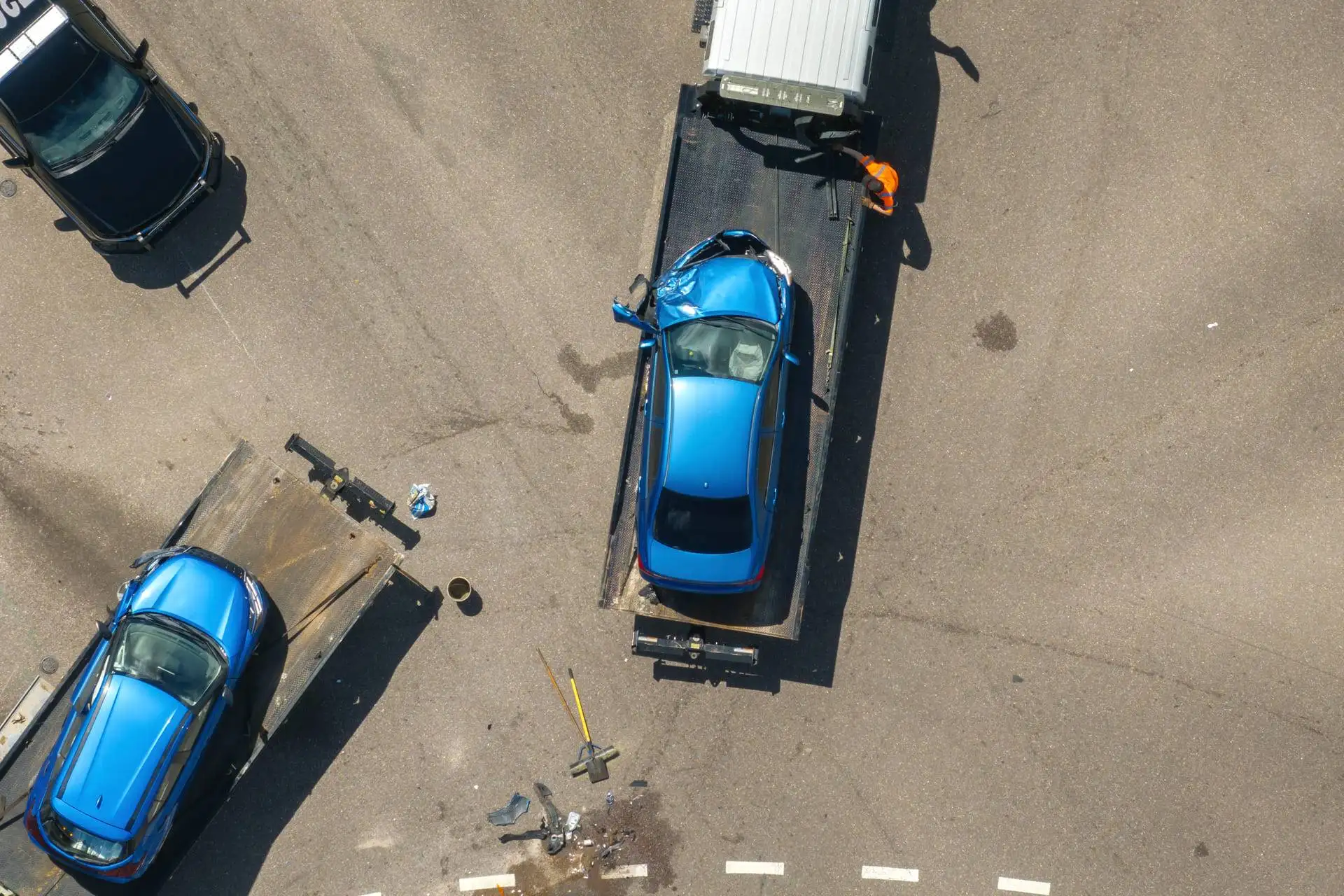Tow truck loading a damaged blue car after an accident, viewed from above