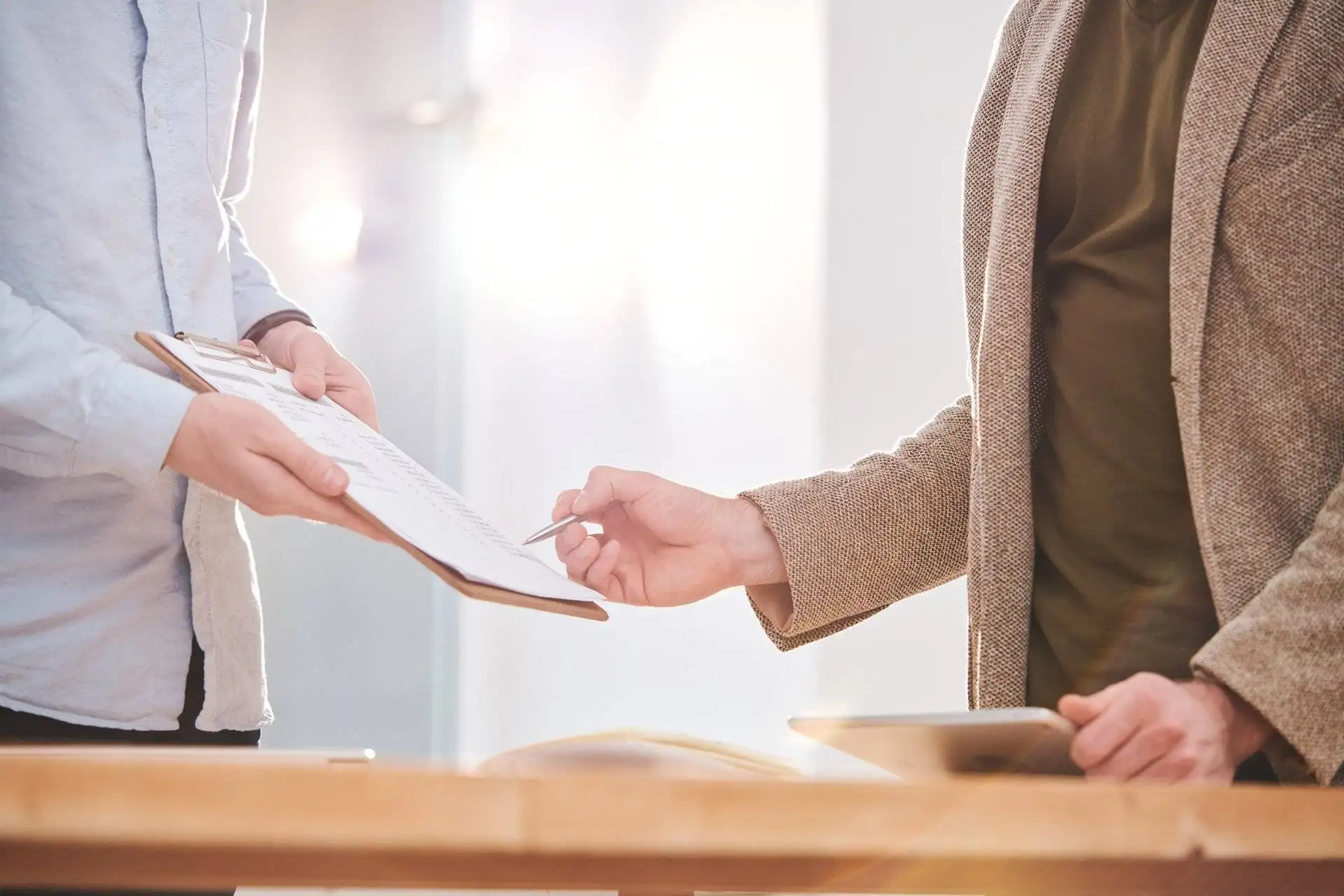 Two people discussing a document on a clipboard at a sunlit desk