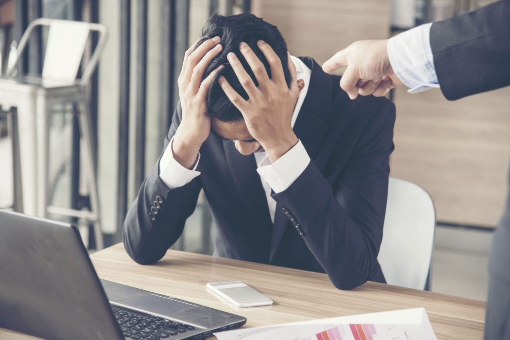 Upset businessman with head in hands while being reprimanded at work