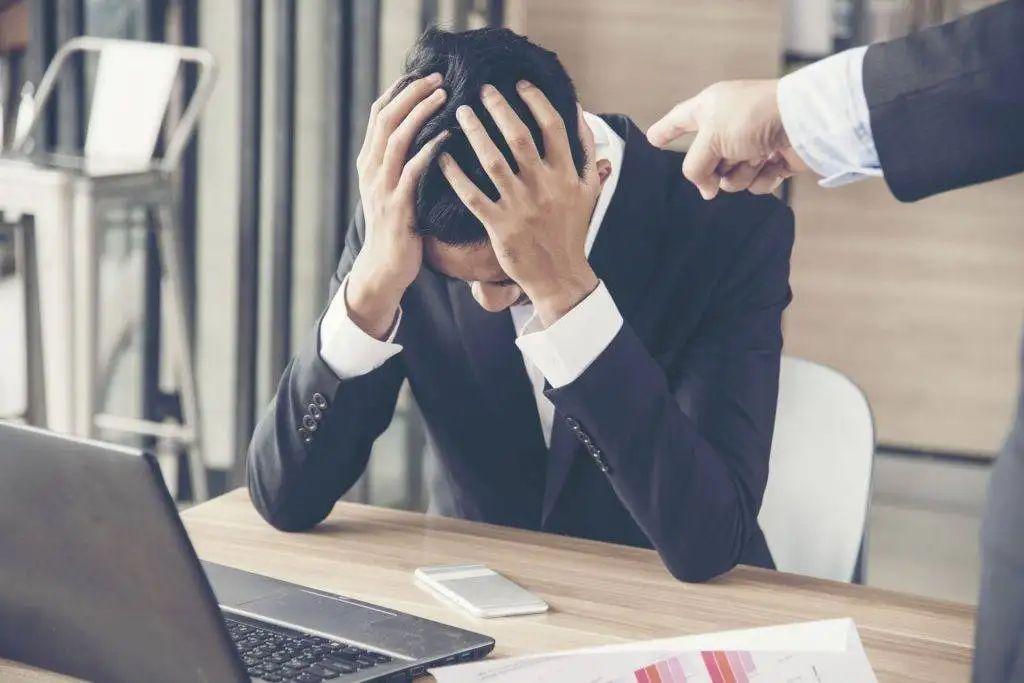 Upset businessman with head in hands while being reprimanded at work