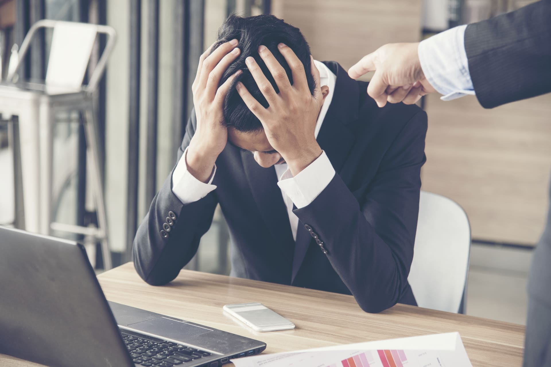 Upset businessman with head in hands while being reprimanded at work