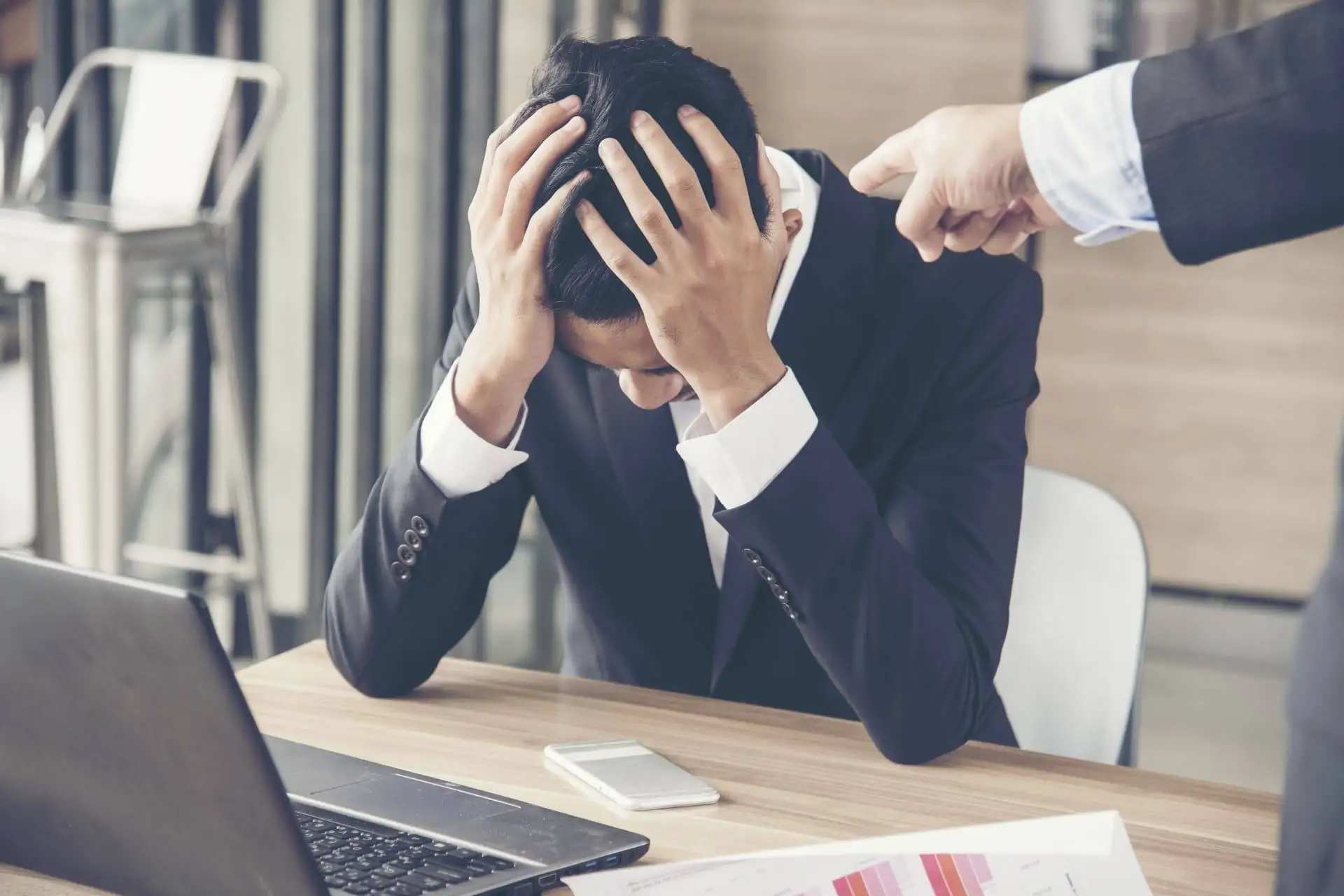 Upset businessman with head in hands while being reprimanded at work