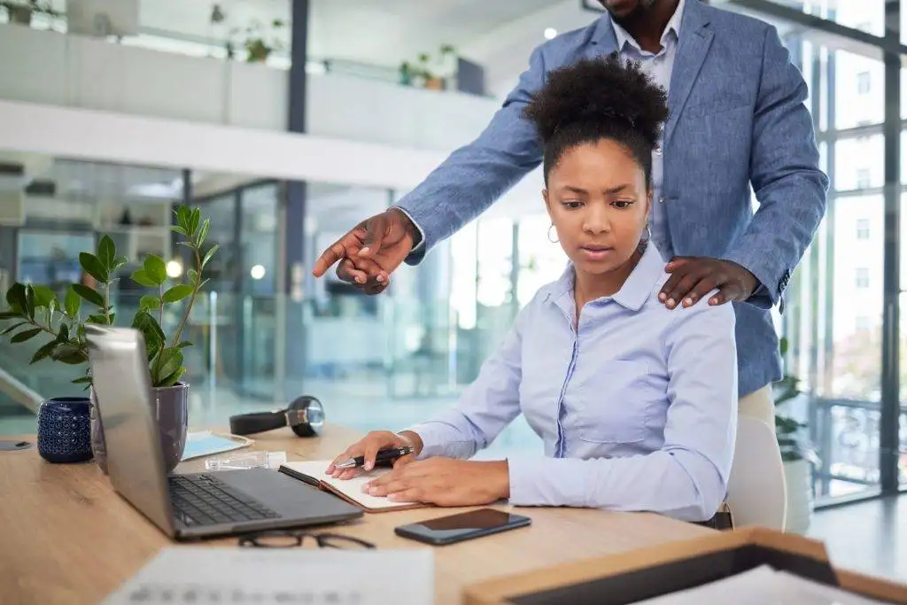 Woman at computer looking uncomfortable as man stands too close behind