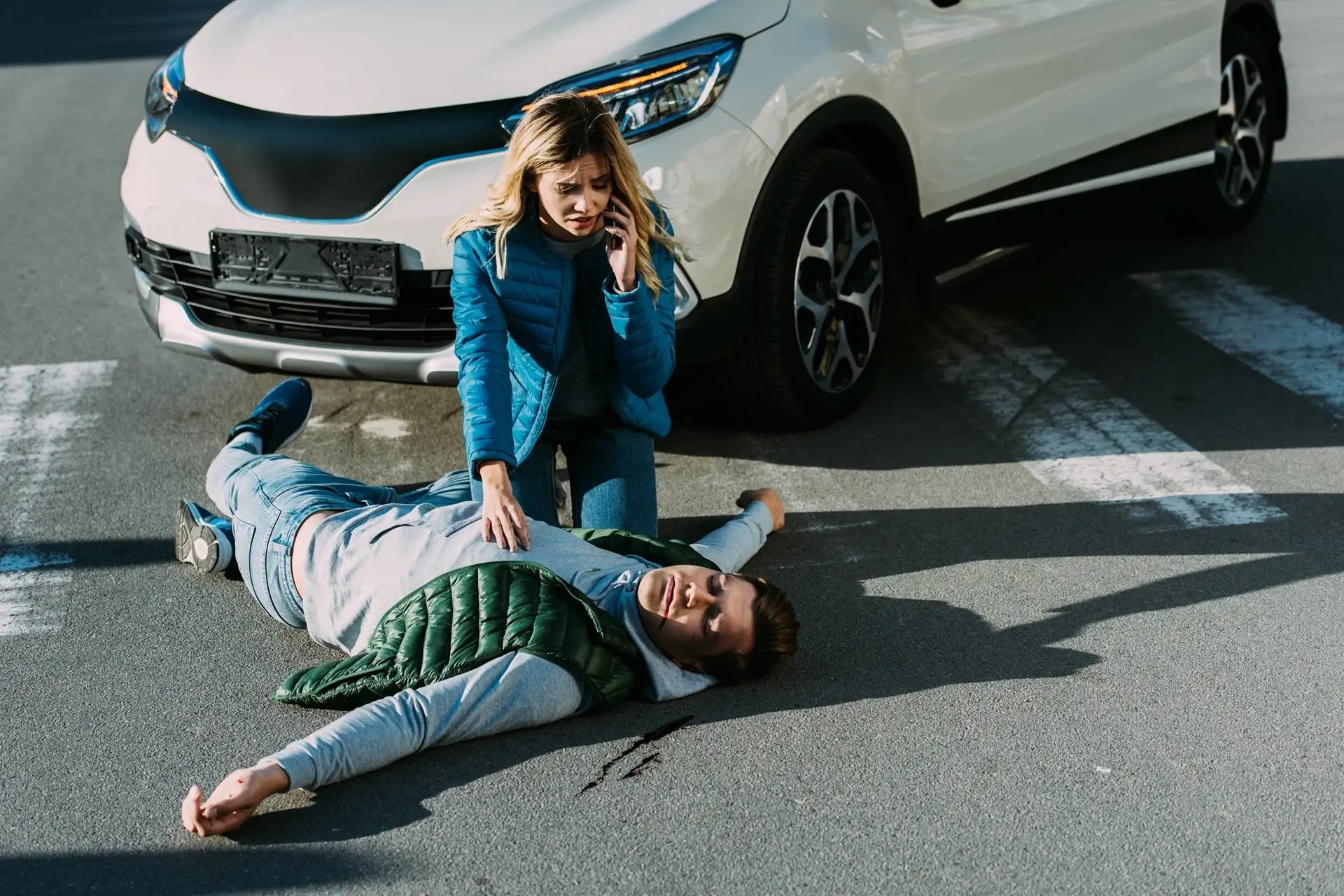 High angle view of scared young woman calling emergency and touching injured man on road after