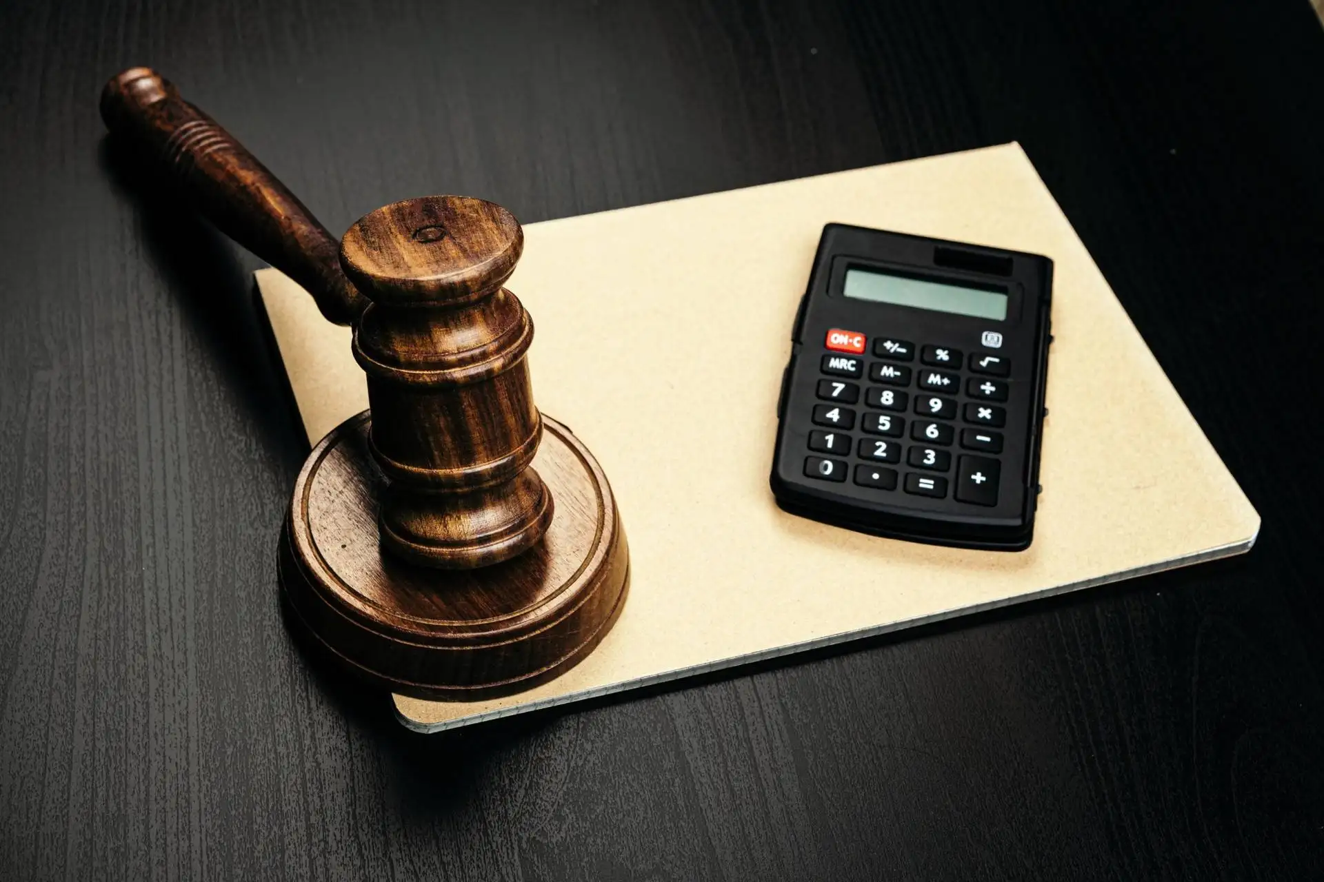 Wooden judge's gavel and calculator on legal document folder