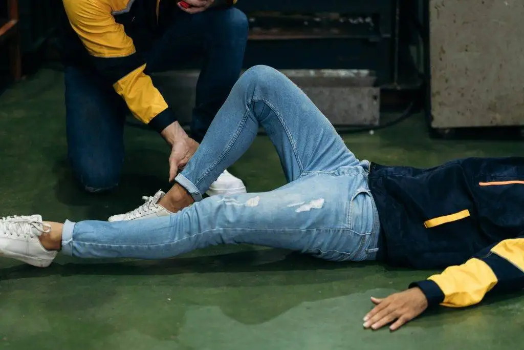 Worker assisting colleague after leg injury in industrial setting