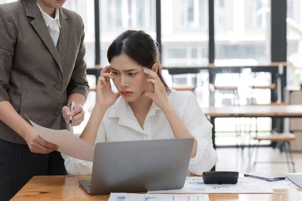 Worried businesswoman looking at documents while working on a laptop