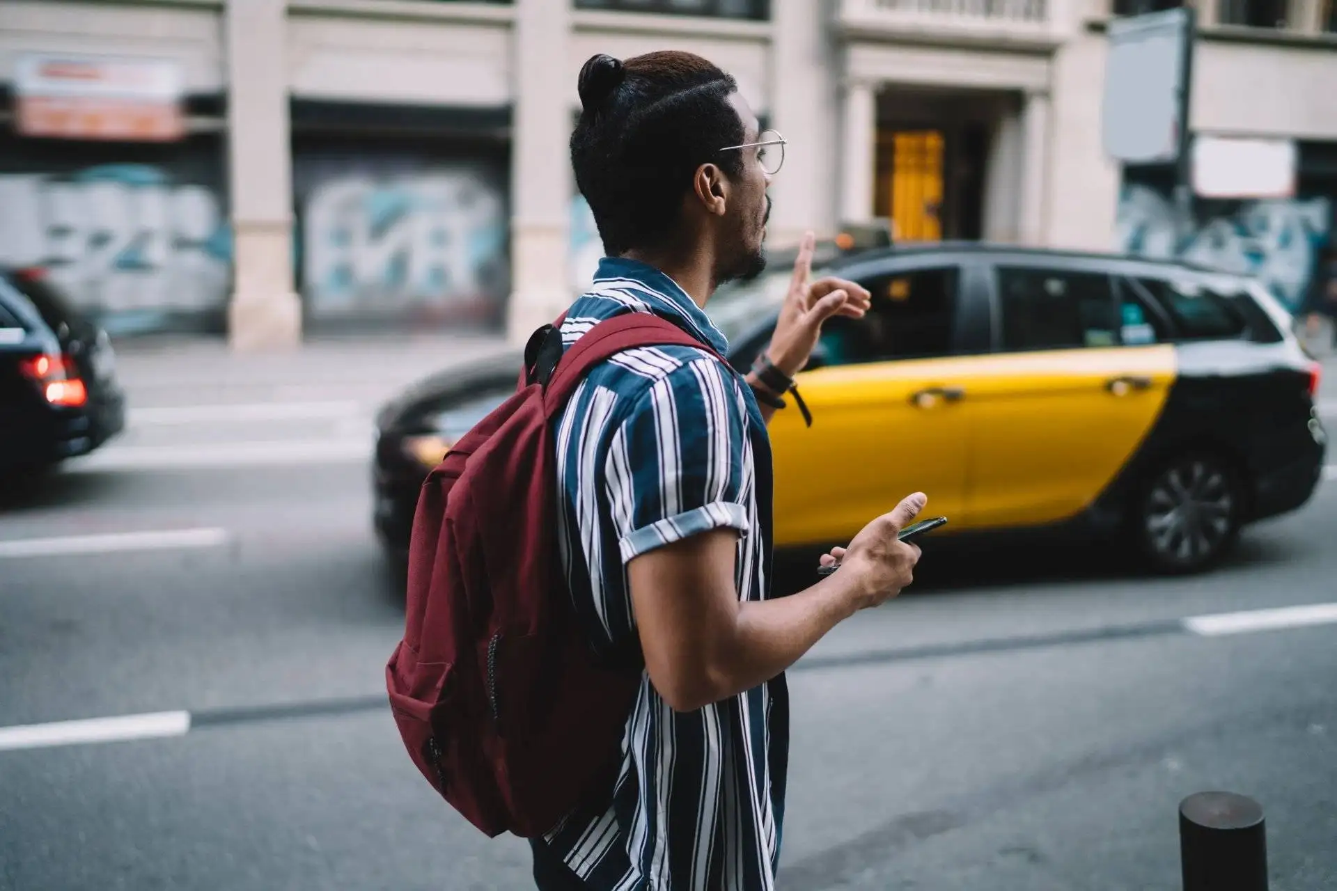 Young man with red backpack signaling for a taxi on a busy road