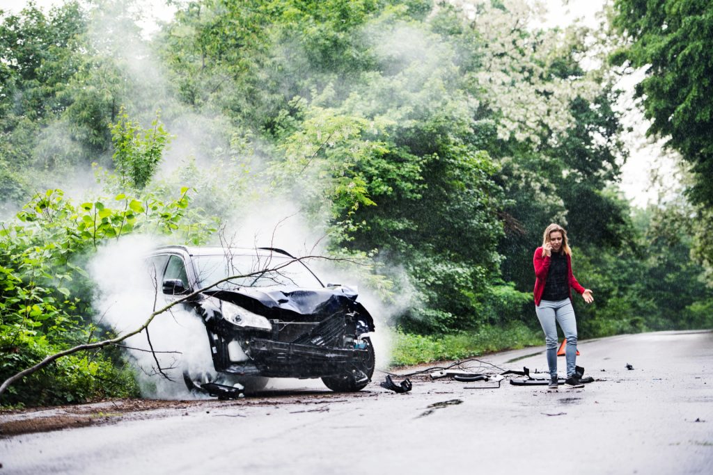 a young woman by a wrecked car in hedge