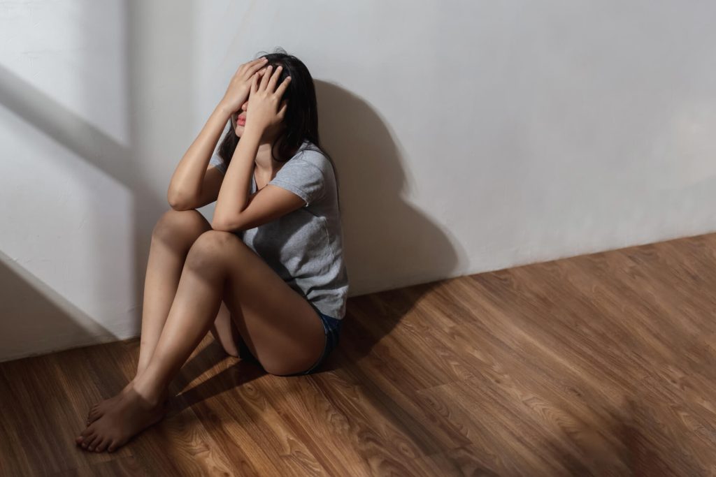 female covering face with hands sitting on the floor