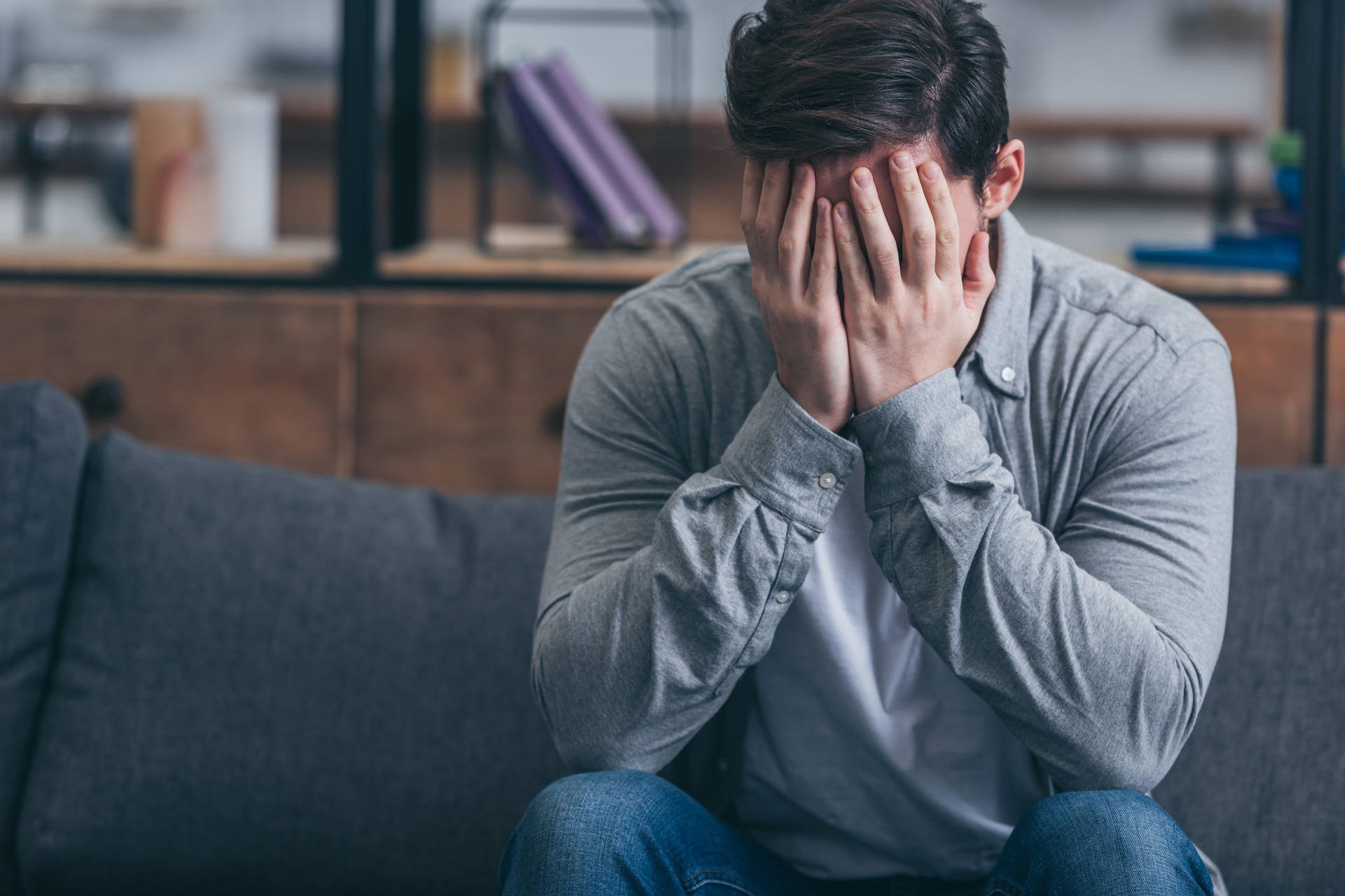 man sitting on couch crying and covering face