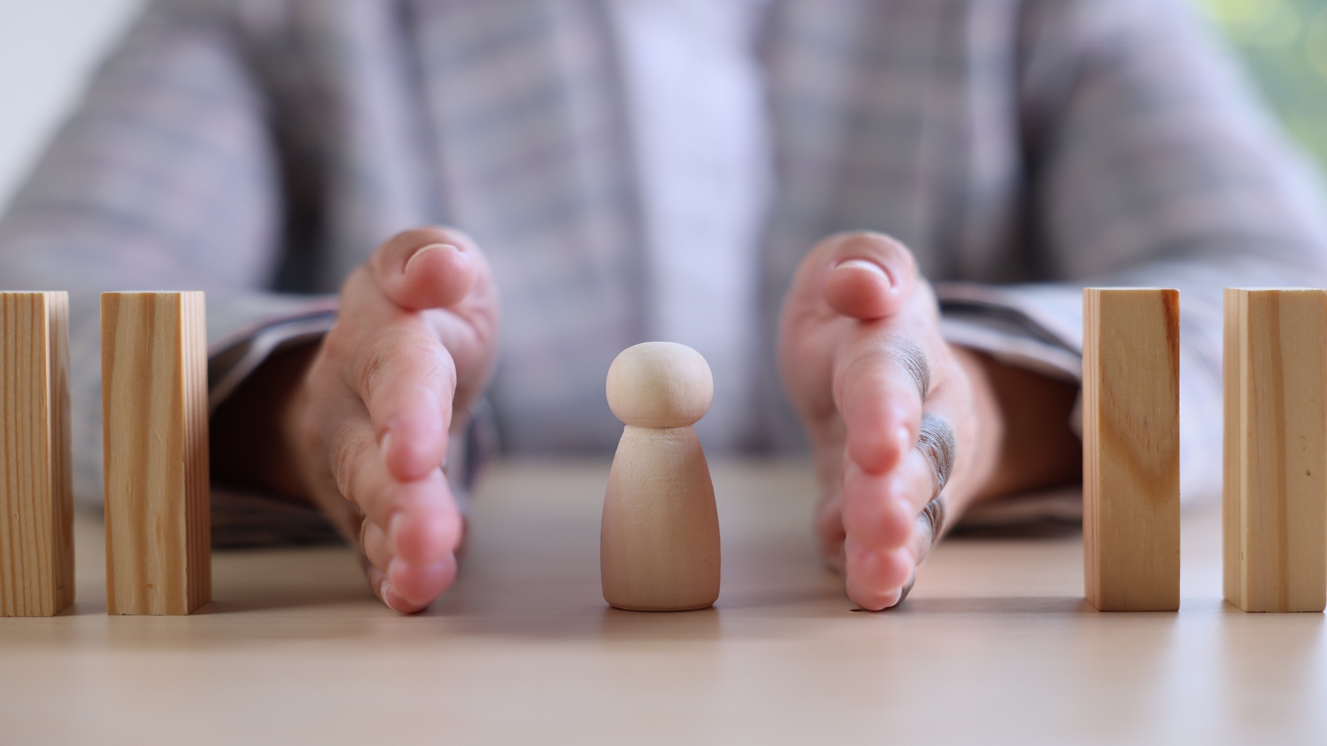 Risk. Woman stopping domino effect to protect wooden figure at table, closeup