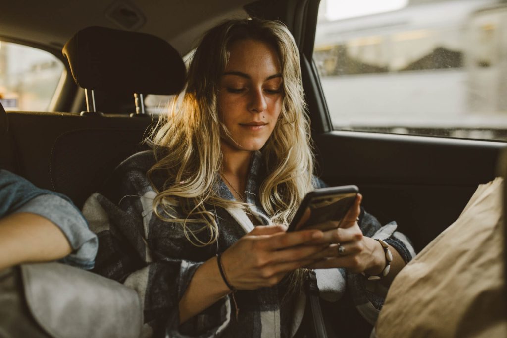 young caucasian woman using smartphone in a rideshare car